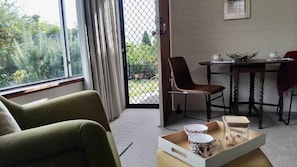 Ein Zimmer mit einem grünen Sessel, einem Esstisch mit Stühlen und einem Fenster mit Vorhängen.