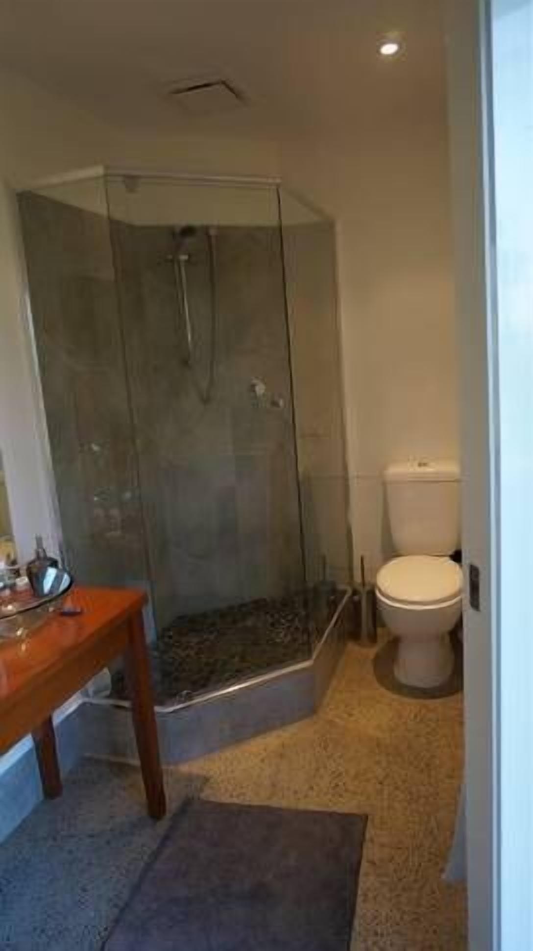 A modern bathroom with a glass-enclosed shower, a toilet, and a wooden vanity.