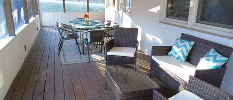 Un patio cubierto con mobiliario de mimbre, una mesa de vidrio y vistas al exterior.