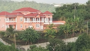 A large, multi-story building with a red roof and white trim, surrounded by lush greenery and hills. - Paradise on the Isle of Spice (Calivigny)