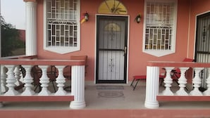A building with a pink facade, two balconies with white balustrades, a grey door with a decorative arch, and barred windows. - Paradise on the Isle of Spice (Calivigny)