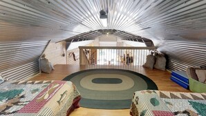 A spacious attic room with a high ceiling, wooden beams, and a large circular rug. - W-W: The Barndominium for Large Groups (Monticello)