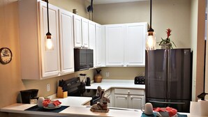 A kitchen with white cabinets, a black refrigerator, a microwave, and a sink. There are two chairs with star patterns and a clock on the wall. - Family Friendly Bahama Bay Condo near Disney (Davenport)