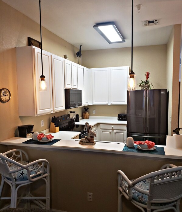 A kitchen with white cabinets, a black refrigerator, a microwave, and a sink. There are two chairs with star patterns and a clock on the wall.