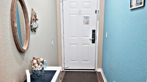 A hallway with a wooden floor, a white door with a doormat, a welcome sign, and a framed sign on the wall. - Family Friendly Bahama Bay Condo near Disney (Davenport)