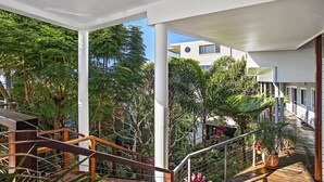 A covered outdoor area with wooden railings, potted plants, and a view of a building in the background. - Jetty Splendour Apartment (Coffs Harbour)