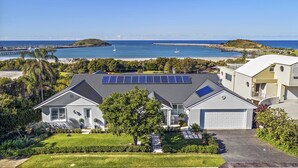 A residential area with houses featuring solar panels, a beach, and a pier in the background. - Jetty Splendour Apartment (Coffs Harbour)