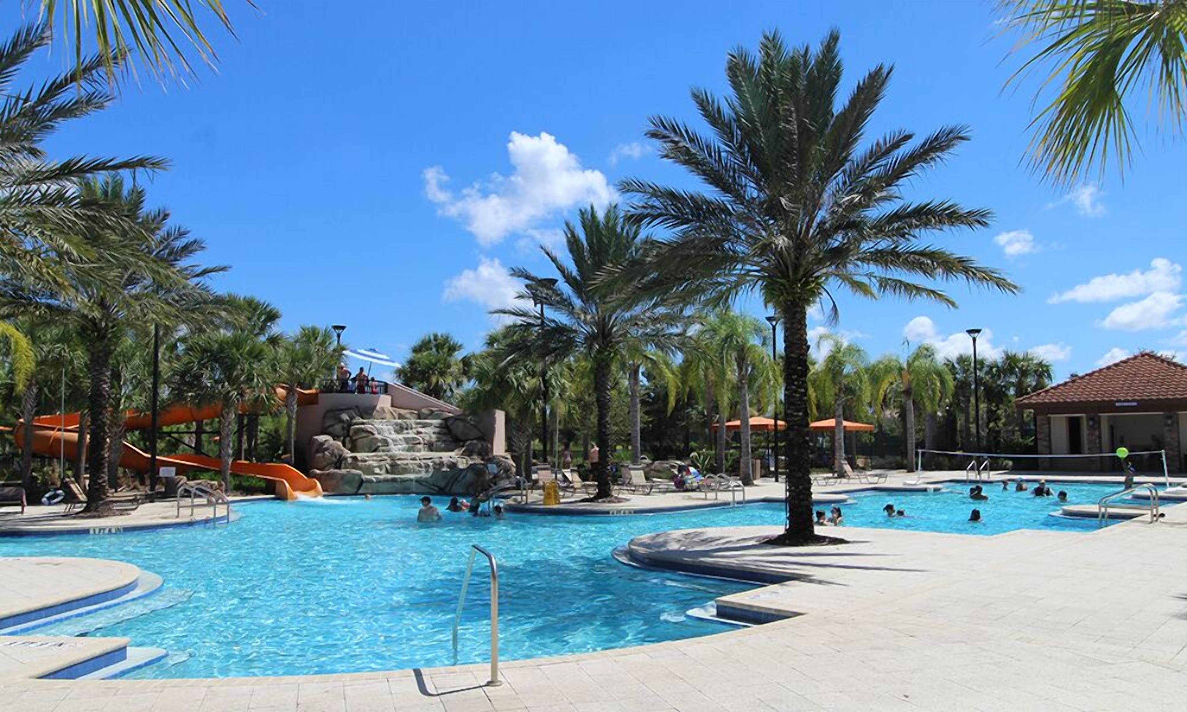A pool area with multiple swimming pools, palm trees, and a water slide.