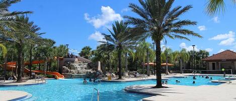 A pool area with multiple swimming pools, palm trees, and a water slide.