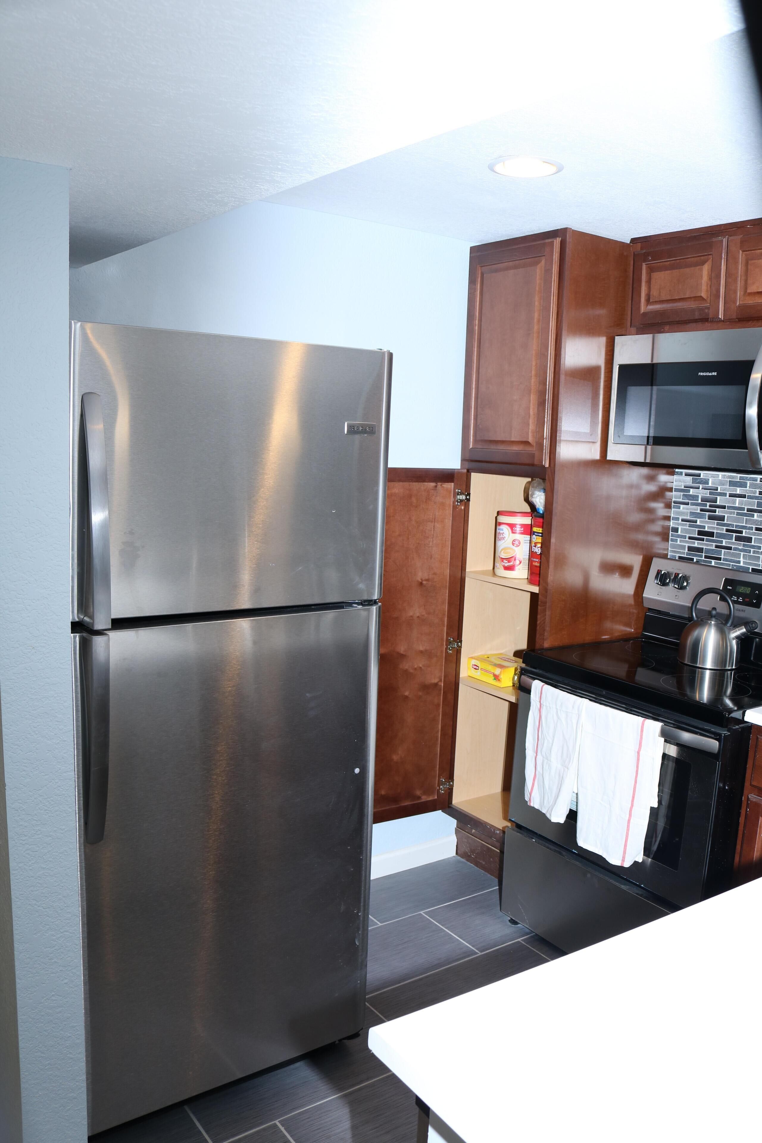 A compact kitchen with a stainless steel refrigerator, a microwave, and a stove.