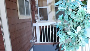 Une façade en bois avec une porte blanche, une petite plante en pot et un panier en osier sur le porche.