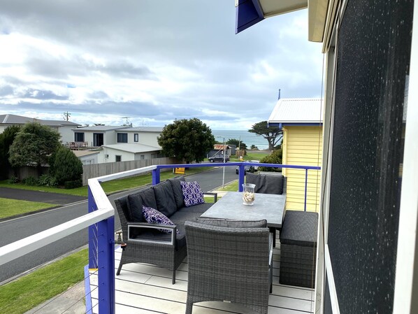 A balcony with wicker furniture, a table, and a view of the street and houses.