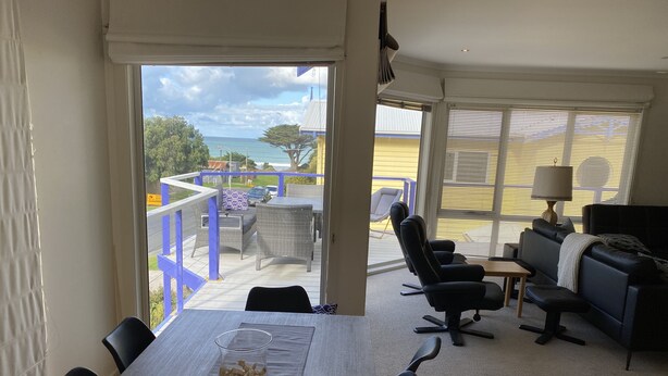 En rummelig opholdsstue med balkon og udsigt over et smukt landskab, møbleret med sofa, stole og et spisebord.