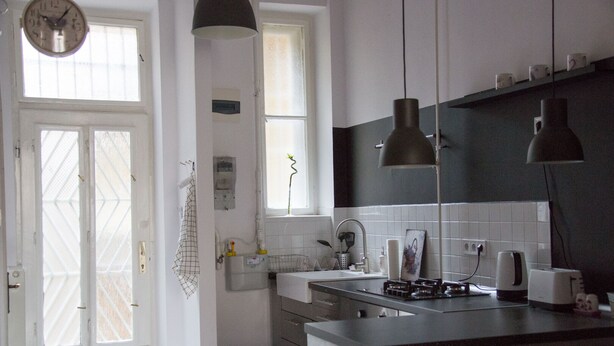 A modern kitchen with a central island, a sink, and a stove. There are hanging lights, a window, and a door with a grid pattern.
