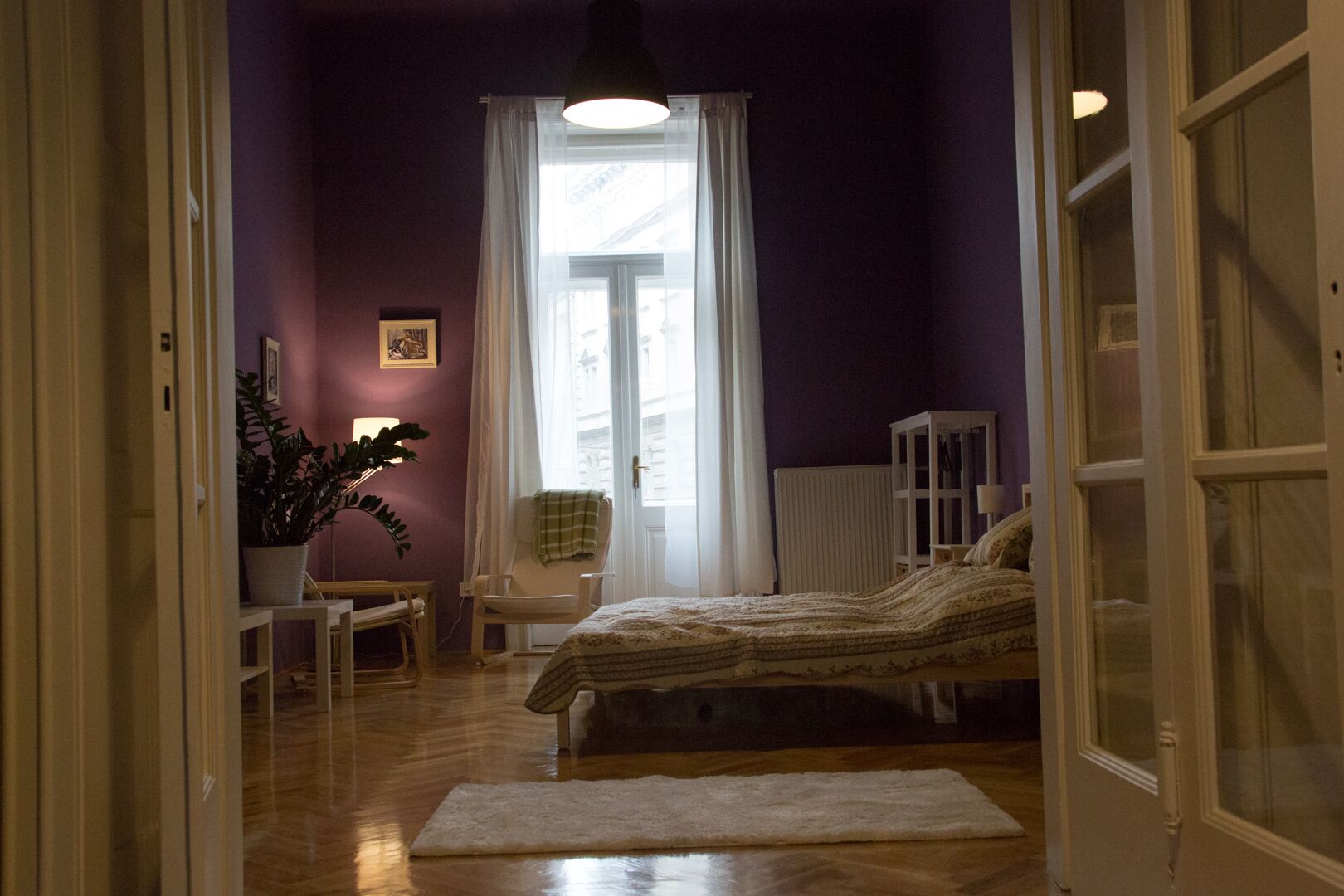 A bedroom with a bed, a chair, a radiator, and a window with curtains.