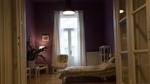 A bedroom with a bed, a chair, a radiator, and a window with curtains.