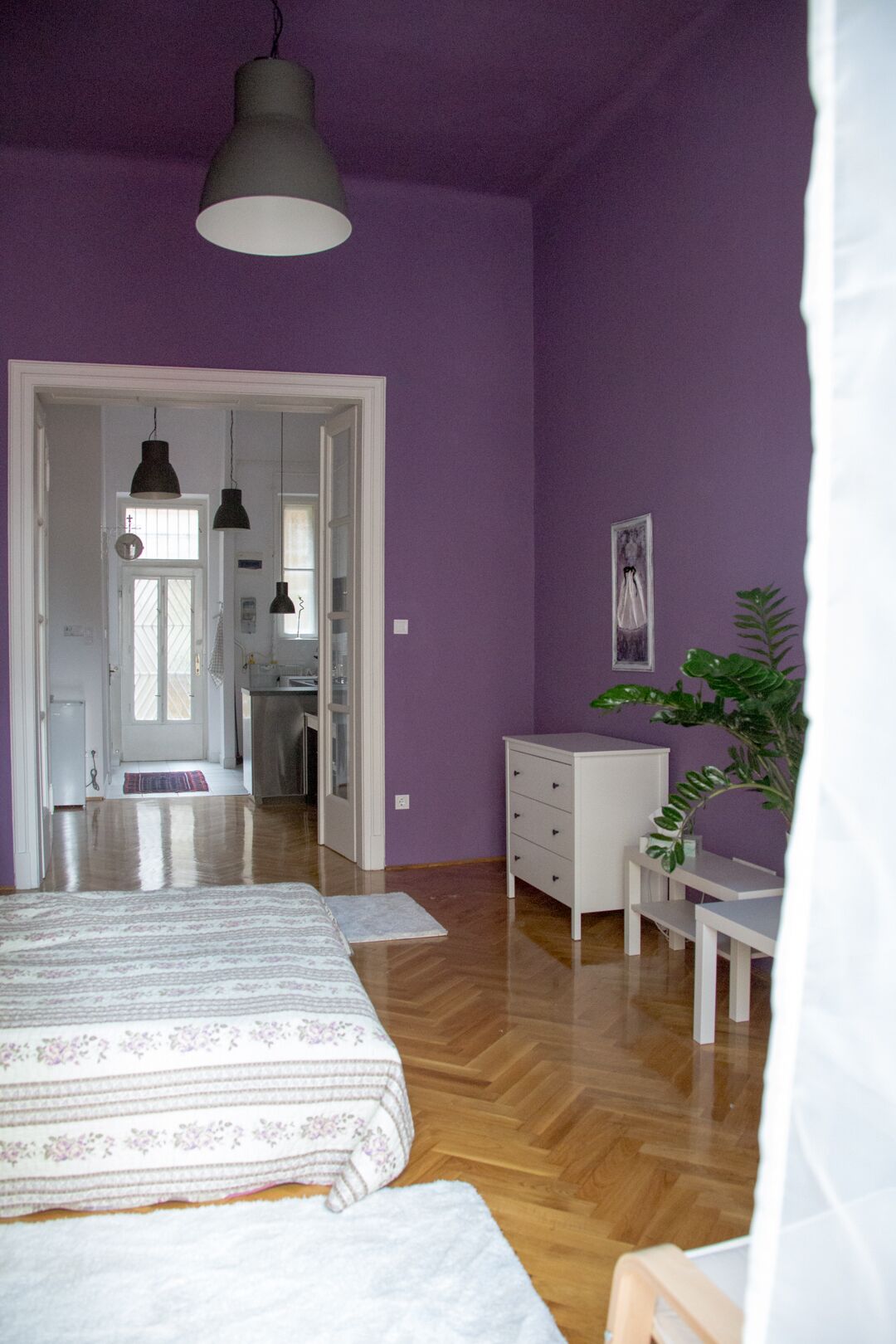 A bedroom with a bed, a dresser, a desk, and a potted plant.