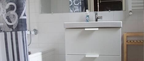 A bathroom with a white sink, a mirror, a shower curtain with numbers, and a blue rug on the floor.
