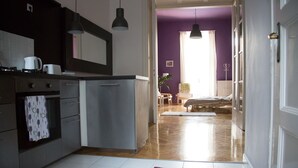 A kitchen with a refrigerator, oven, and a sink. There is a dining area with a table and chairs, and a bed in the background.
