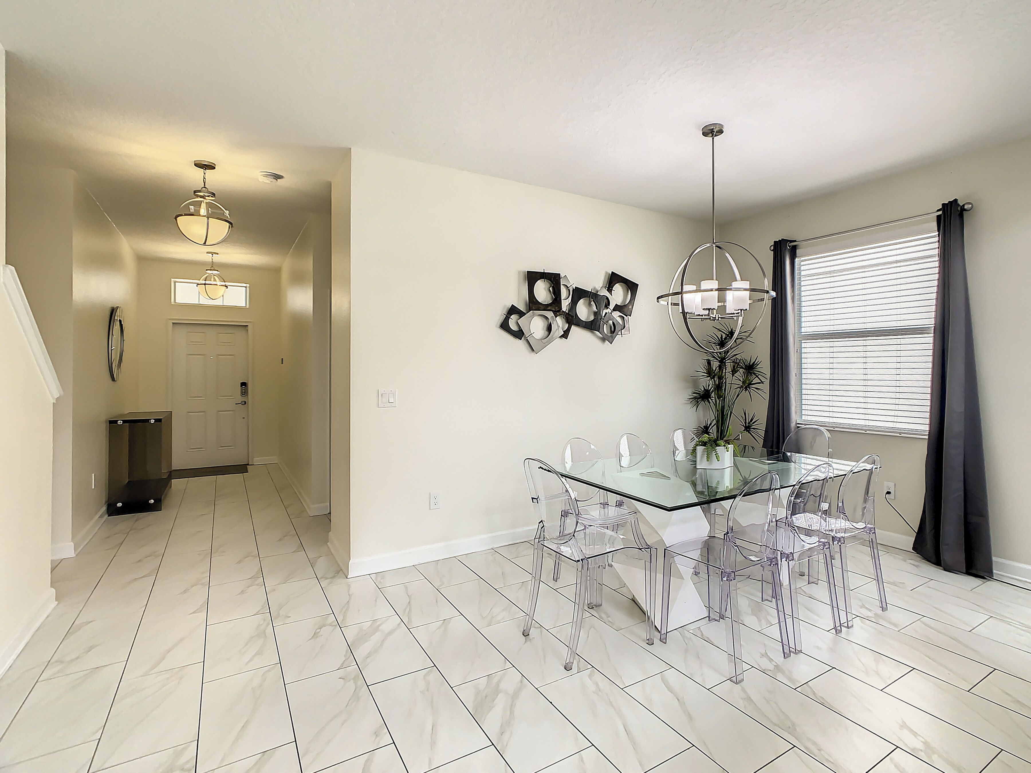 A modern dining area with a glass table and chairs, a chandelier, and a potted plant.