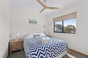 Une chambre à coucher comprenant un lit, une table de chevet, un ventilateur de plafond, une fenêtre avec vue et des œuvres d’art mural.
