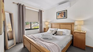 A neatly arranged bedroom with a bed, bedside tables, a mirror, and a window with curtains.