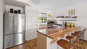 A modern kitchen with a stainless steel refrigerator, wooden bar stools, and a built-in island.