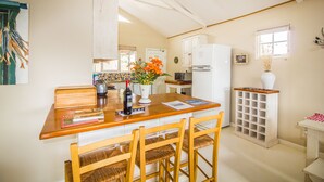 Una cocina con una mesa de madera, sillas, un refrigerador, un ventanal y un florero con flores.