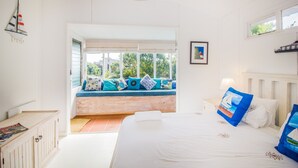 Un dormitorio con cama, un asiento junto a la ventana con cojines, una mesita y un estante en la pared.