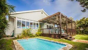 Una propiedad residencial con piscina, un patio cubierto y una casa con ventanas amplias.
