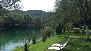 A grassy area with a white lounge chair by a lake, surrounded by trees and a picnic table. - Peaceful Oasis - House For Rest And Relaxation (Bosanska Krupa)
