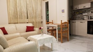 A living room with a beige sofa, a small table with a vase of flowers, and a kitchen area with cabinets and a tiled backsplash. - BRIGHT APARTMENT LINGOTTO FIERE - OLYMPIC STADIUM (Torino)