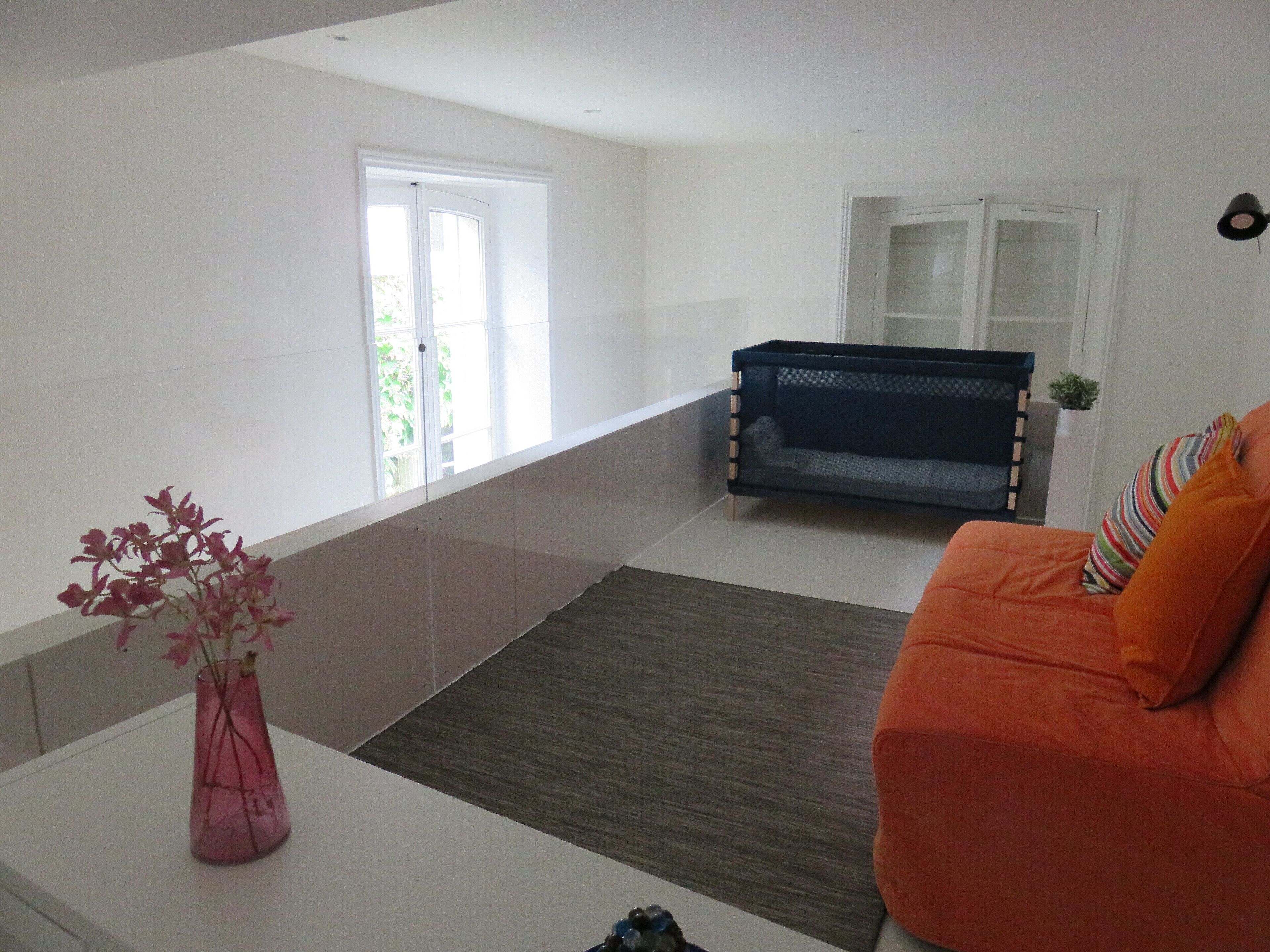 A living room with a sofa, a small table with a vase, a window, and a door.