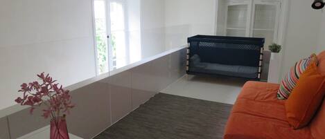 A living room with a sofa, a small table with a vase, a window, and a door.