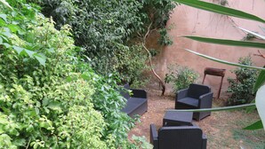 A patio area with wicker furniture, surrounded by dense foliage and a rustic wall. - Quite apartment on garden, ideally located in the heart of La Rochelle (La Rochelle)