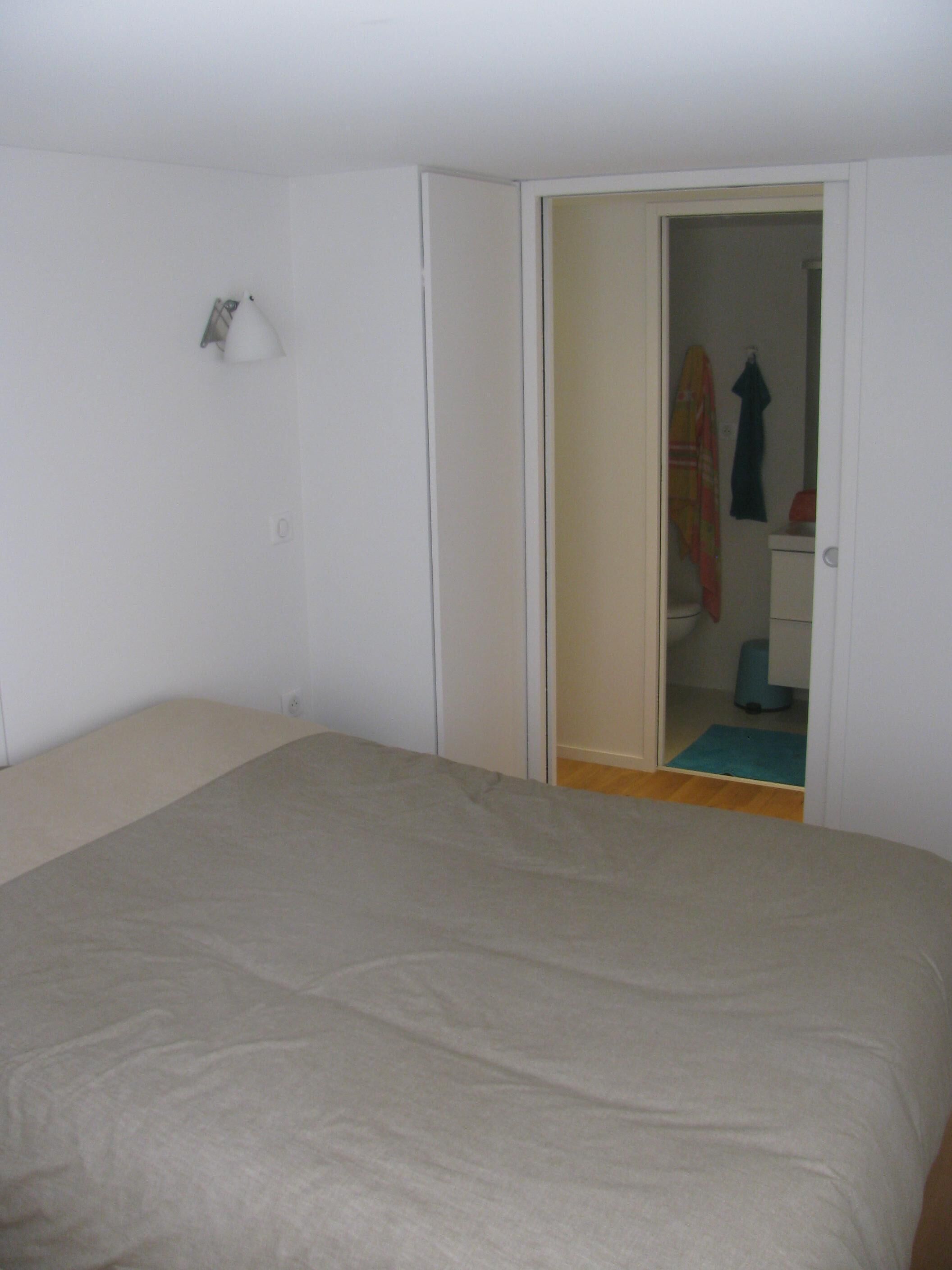Una camera da letto con un letto, una porta che dà su un bagno e un tavolino con una lampada.