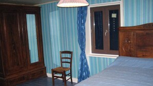 Une chambre à coucher avec un lit en bois, une chaise en bois, une fenêtre avec des rideaux et une armoire en bois.