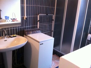 Een compacte badkamer met een witte wastafel, een kleine wasmachine en een douchehoek.