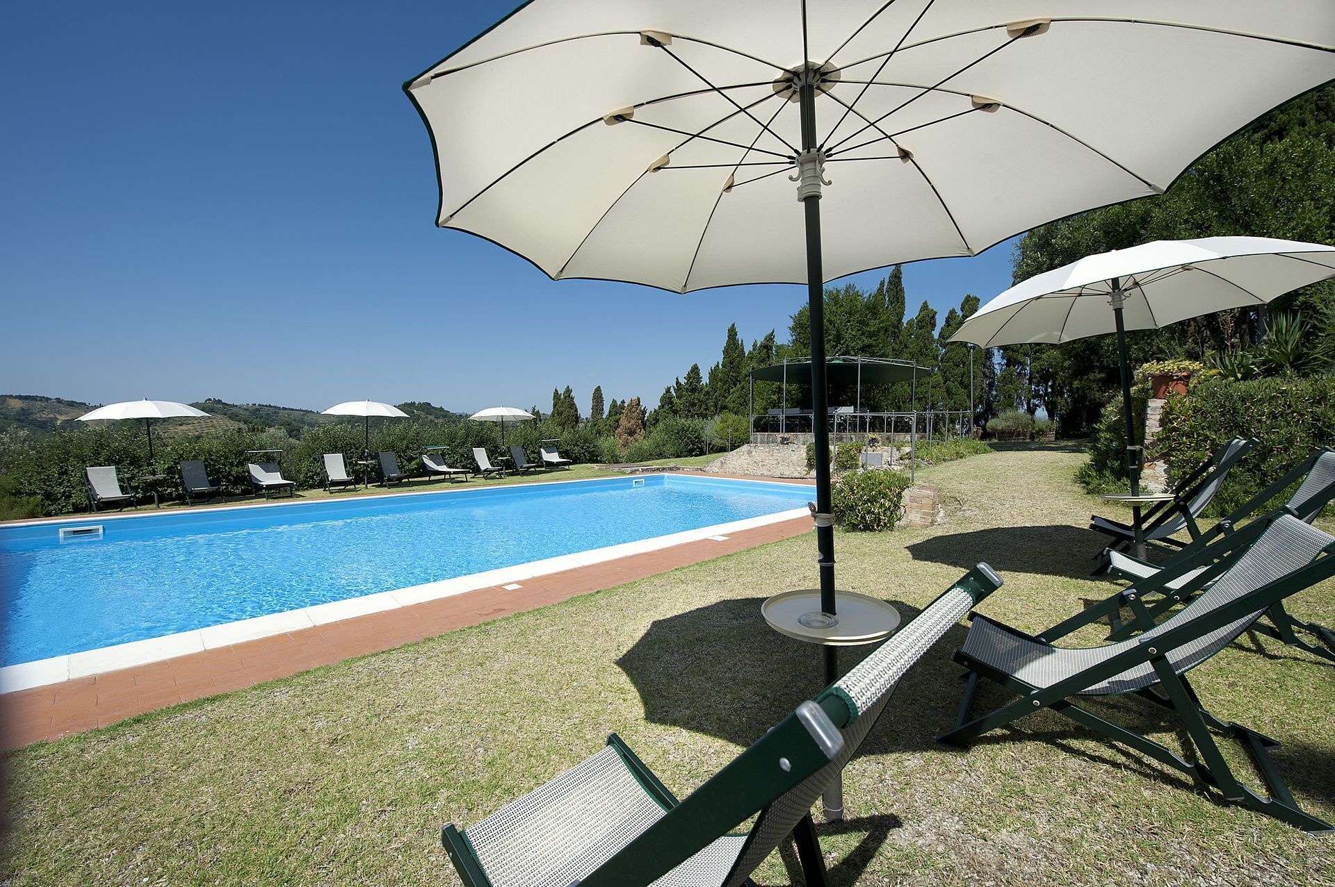 Zona junto a la piscina con piscina, sillas de descanso y sombrillas.
