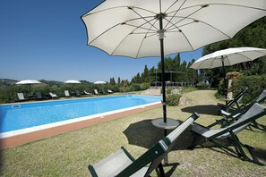 Zona junto a la piscina con piscina, sillas de descanso y sombrillas.
