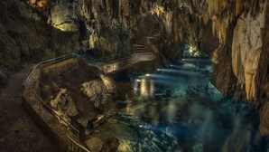 Una cueva con un arroyo, una escalera y una barandilla.