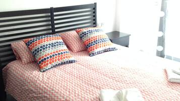 Een net opgemaakt bed met een bedspread met patroon en kussens, een zwart hoofdbord, een nachtkastje met een lamp en een raam met gordijnen.