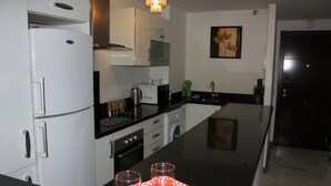 Een moderne keuken met een koelkast, oven, magnetron en spoelbak. Er staan twee glazen op een dienblad en er hangt een schilderij aan de muur.