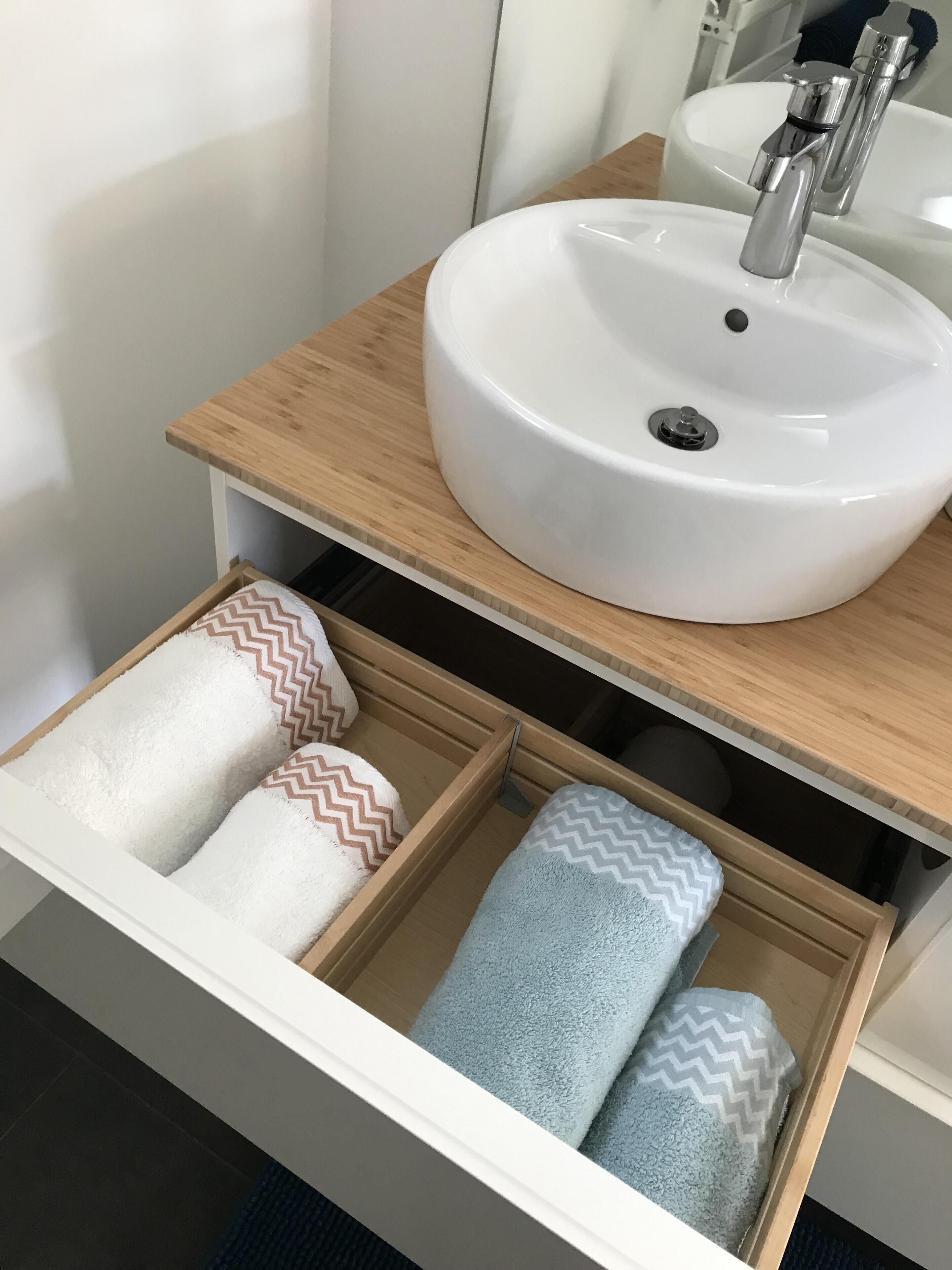 A bathroom with a white sink, wooden countertop, and a towel drawer with patterned towels.