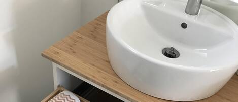 A bathroom with a white sink, wooden countertop, and a towel drawer with patterned towels.