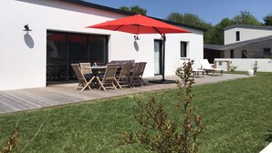 Una casa moderna con patio attrezzato, tavolo e sedie sotto un ombrellone rosso.