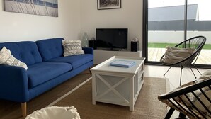 Un soggiorno con un divano blu, una televisione, un tavolino da caffè e una poltrona in vimini.