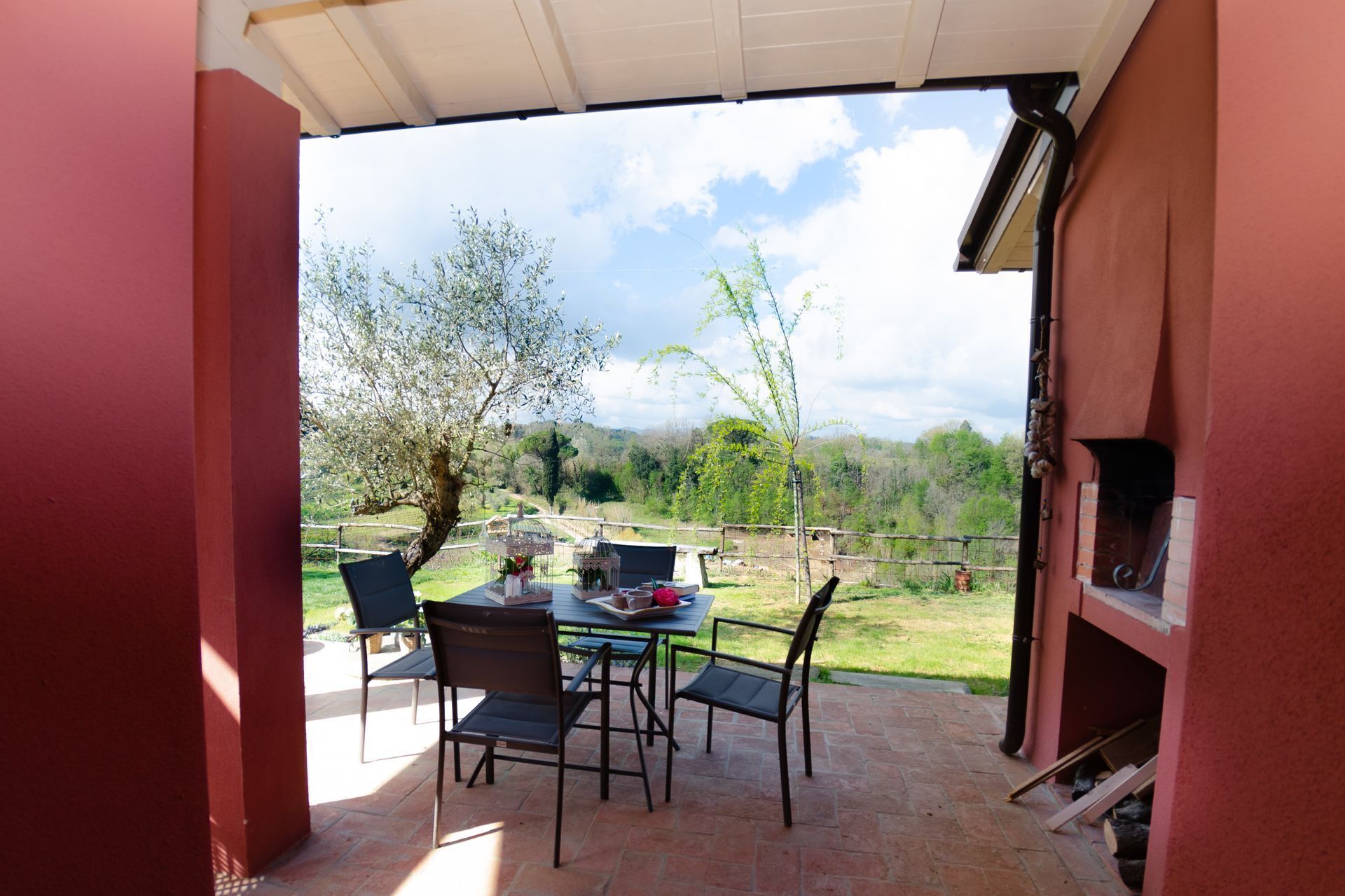 An outdoor patio with a table and chairs, a grill, and a view of a green landscape.