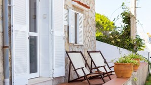 Un edificio de piedra con contraventanas blancas, un patio adoquinado y dos sillones.