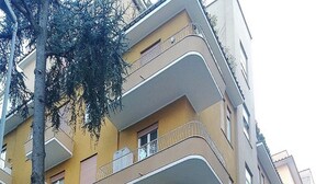 Un edifici residencial de diverses plantes amb balcons, un mur de maó i cotxes aparcats.